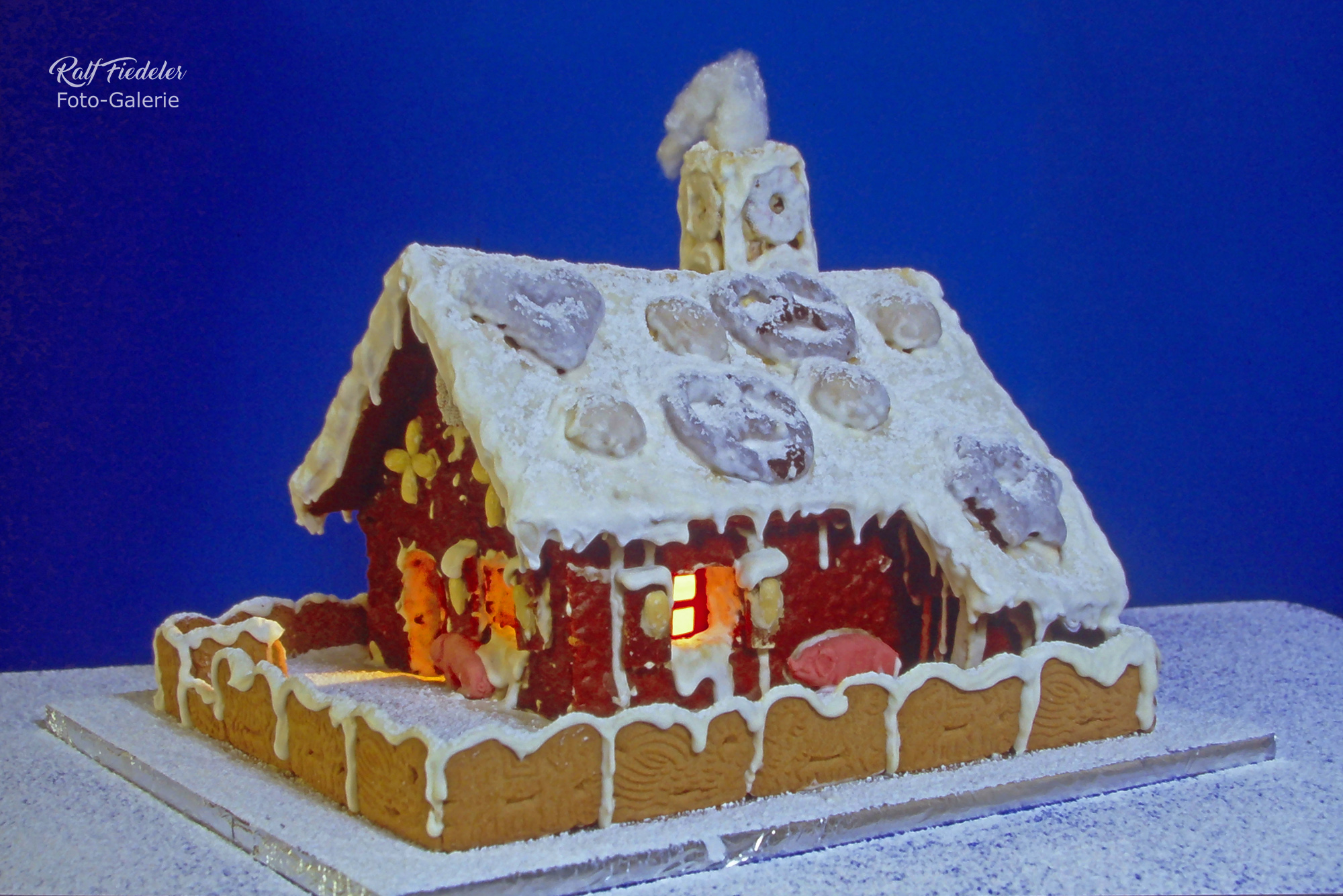 Mein selbstgebautes Pfefferkuchenhaus vor blauem Hintergrund mit Puderzuckerschnee