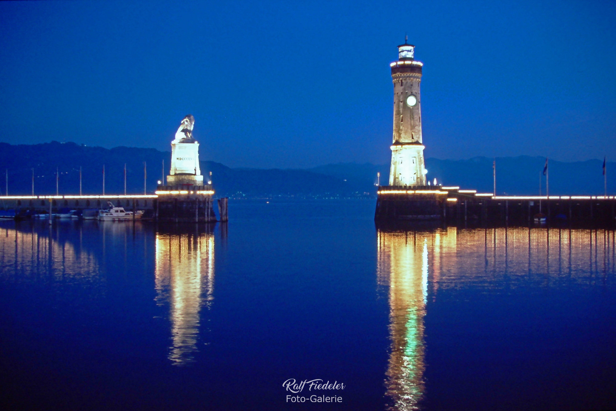 Beleuchtete Hafeneinfahrt von Lindau mit dem Löwen und dem Leuchtturm in der blauen Stunde